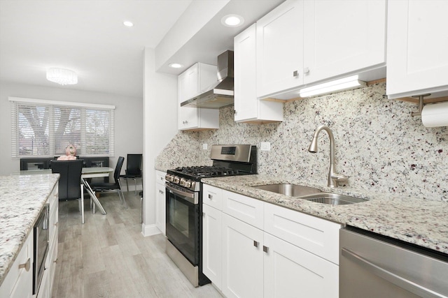 kitchen with sink, white cabinetry, stainless steel appliances, and wall chimney range hood