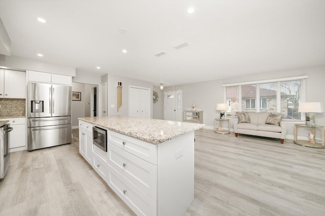 kitchen featuring light stone countertops, light hardwood / wood-style flooring, white cabinets, and appliances with stainless steel finishes