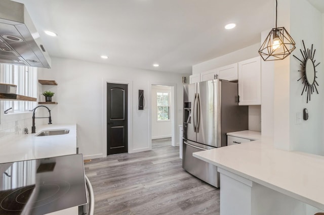 kitchen featuring sink, wall chimney range hood, stainless steel fridge with ice dispenser, decorative light fixtures, and white cabinets