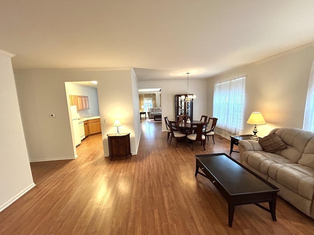 living area featuring a wealth of natural light, light wood-type flooring, a chandelier, and baseboards