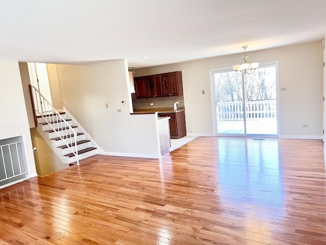 unfurnished living room featuring a notable chandelier and light wood-type flooring