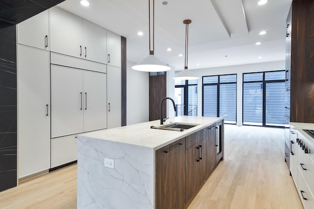 kitchen with white cabinetry, sink, an island with sink, pendant lighting, and light hardwood / wood-style floors