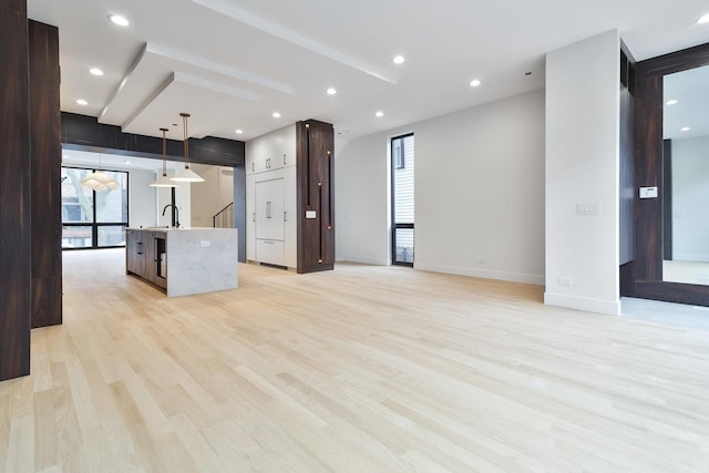 kitchen featuring sink, hanging light fixtures, light stone countertops, light wood-type flooring, and an island with sink