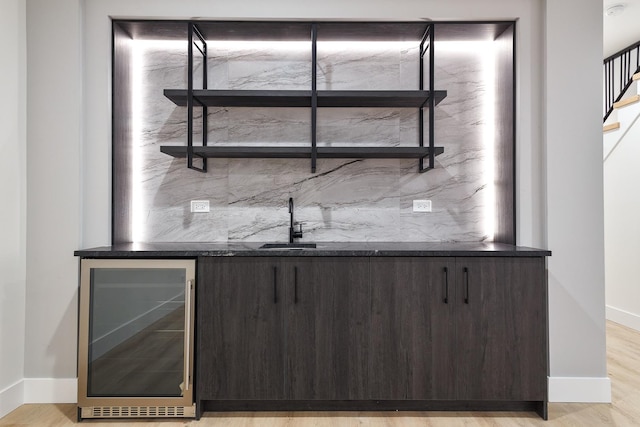 bar with dark brown cabinets, light hardwood / wood-style flooring, wine cooler, and sink