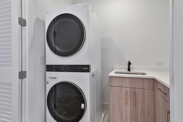 clothes washing area with cabinets, stacked washing maching and dryer, and sink