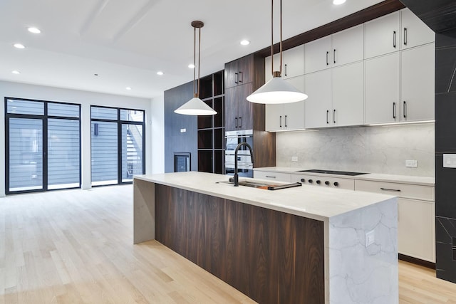 kitchen with pendant lighting, sink, decorative backsplash, an island with sink, and dark brown cabinets