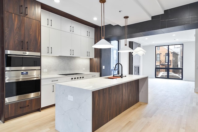 kitchen featuring dark brown cabinetry, sink, a healthy amount of sunlight, pendant lighting, and a center island with sink