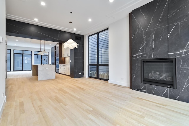 kitchen featuring a kitchen island with sink, sink, a premium fireplace, decorative light fixtures, and light hardwood / wood-style floors