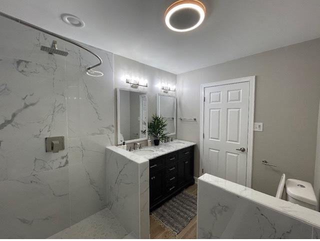 bathroom with tiled shower, vanity, and toilet