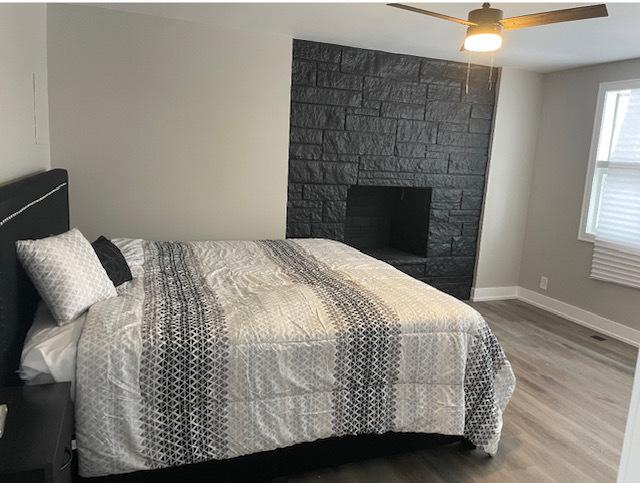 bedroom featuring ceiling fan, hardwood / wood-style flooring, and a fireplace