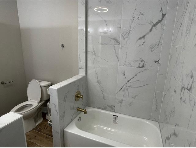 bathroom featuring hardwood / wood-style flooring, toilet, and tiled shower / bath