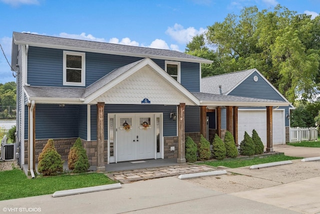 traditional-style house with covered porch, stone siding, roof with shingles, and a garage