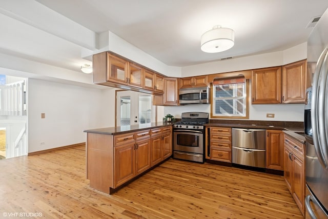 kitchen with a peninsula, light wood-style flooring, appliances with stainless steel finishes, and brown cabinets