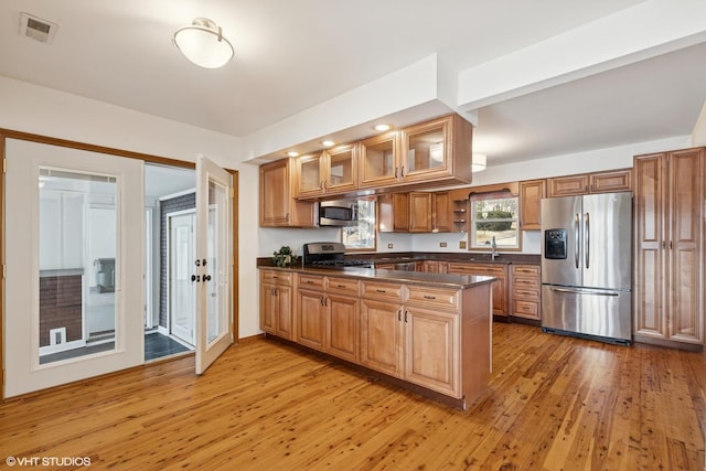 kitchen featuring stainless steel appliances, dark countertops, brown cabinetry, light wood-type flooring, and a peninsula