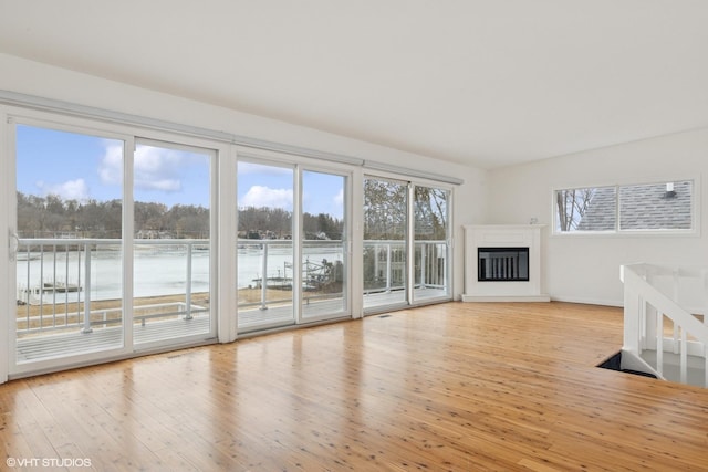 unfurnished living room featuring wood-type flooring, baseboards, and a glass covered fireplace