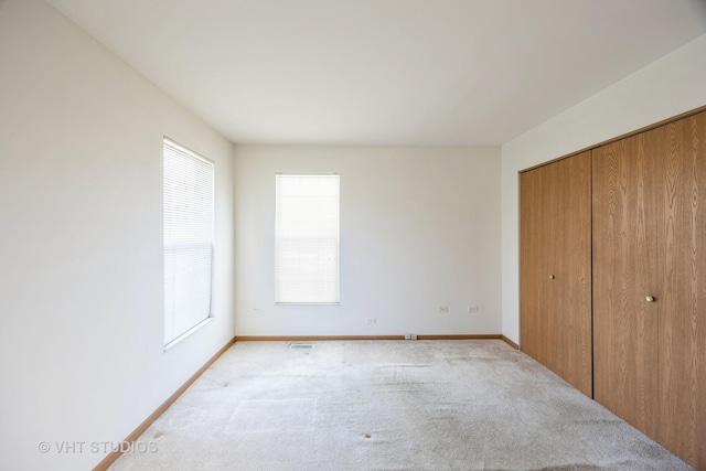 unfurnished bedroom with multiple windows, light carpet, and a closet