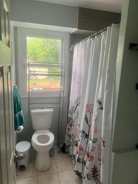 bathroom with a shower with shower curtain, tile patterned floors, and toilet