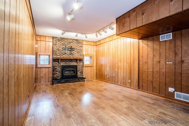 unfurnished living room with wood-type flooring, rail lighting, wooden walls, and a brick fireplace