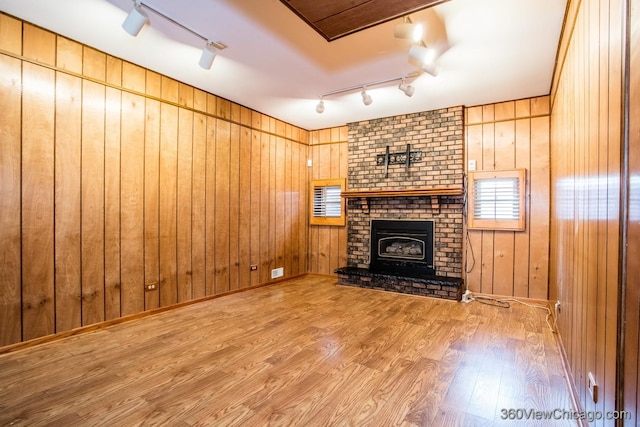 unfurnished living room with rail lighting, wooden walls, and a brick fireplace