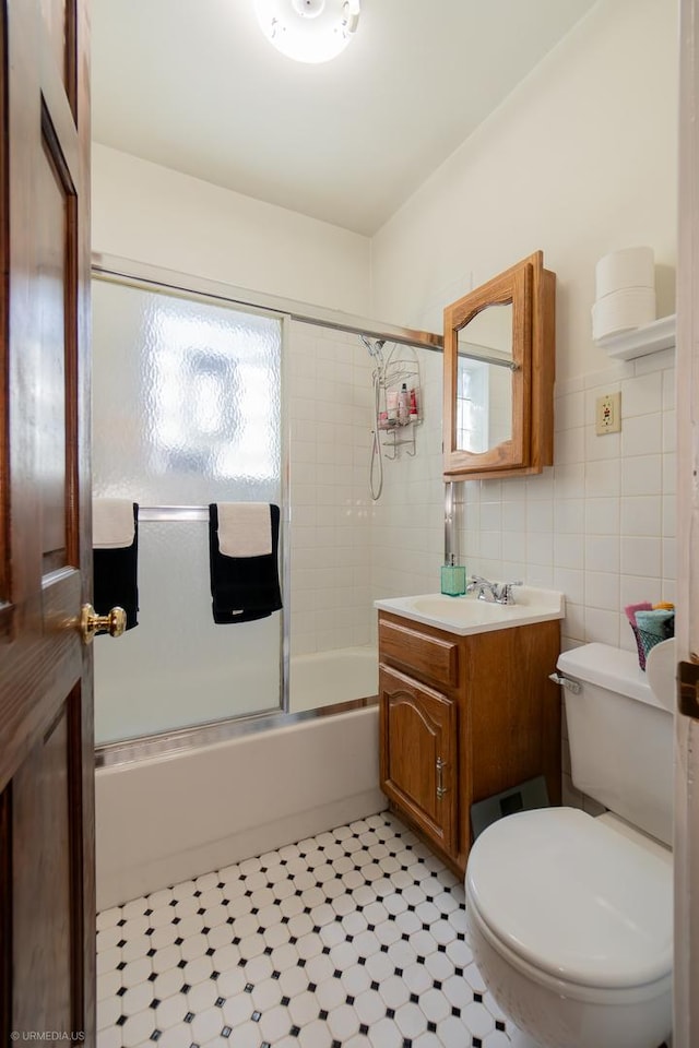 full bathroom with vanity, shower / bath combination with glass door, tile walls, tile patterned flooring, and toilet