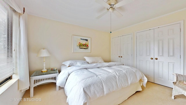 carpeted bedroom featuring ornamental molding, two closets, and ceiling fan