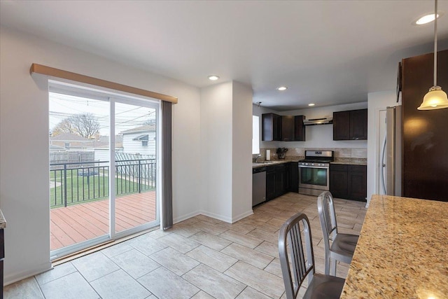 kitchen with sink, dark brown cabinets, hanging light fixtures, appliances with stainless steel finishes, and light stone countertops