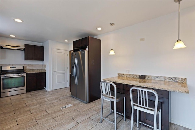 kitchen with stainless steel appliances, light stone countertops, dark brown cabinetry, and decorative light fixtures