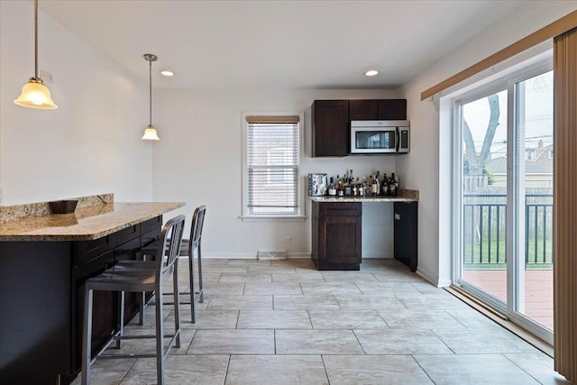 kitchen with decorative light fixtures, light stone counters, dark brown cabinetry, and a wealth of natural light