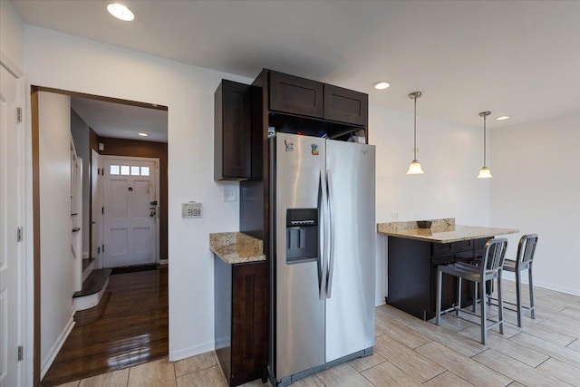 kitchen featuring a kitchen bar, decorative light fixtures, dark brown cabinets, stainless steel fridge, and light stone countertops