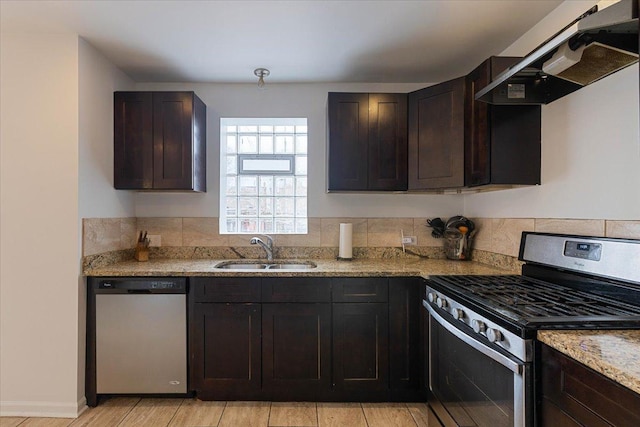 kitchen featuring sink, appliances with stainless steel finishes, range hood, dark brown cabinetry, and light stone countertops