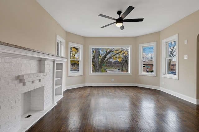 unfurnished living room featuring a fireplace, built in features, ceiling fan, and dark wood-type flooring