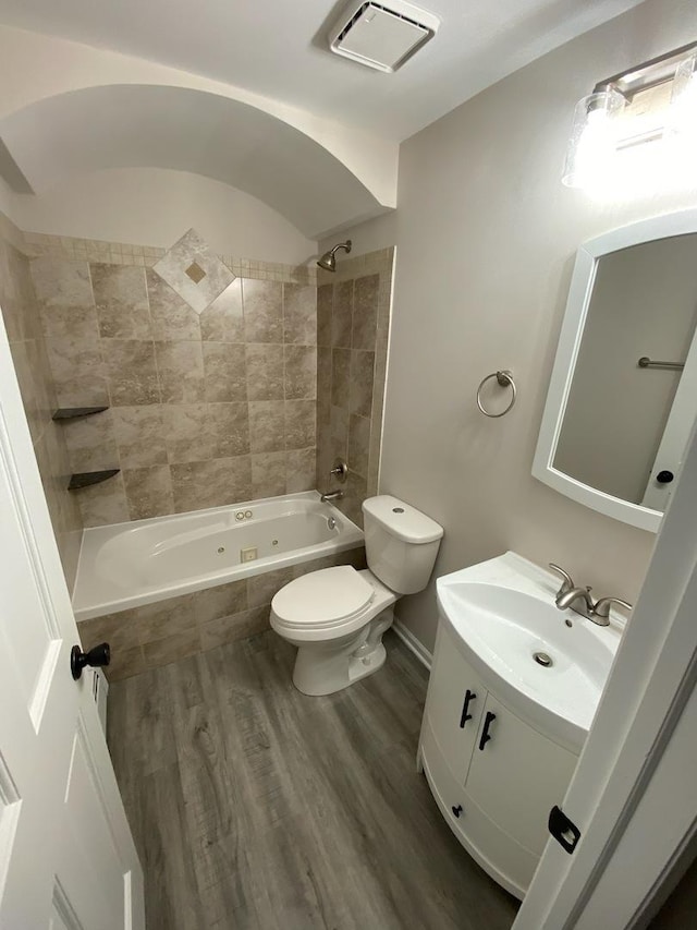 full bathroom featuring hardwood / wood-style flooring, tiled shower / bath combo, toilet, and vanity