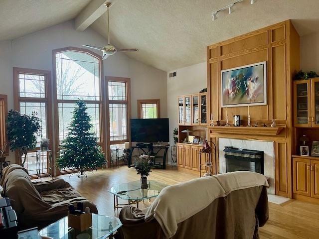 living room with ceiling fan, lofted ceiling with beams, a textured ceiling, and light hardwood / wood-style floors