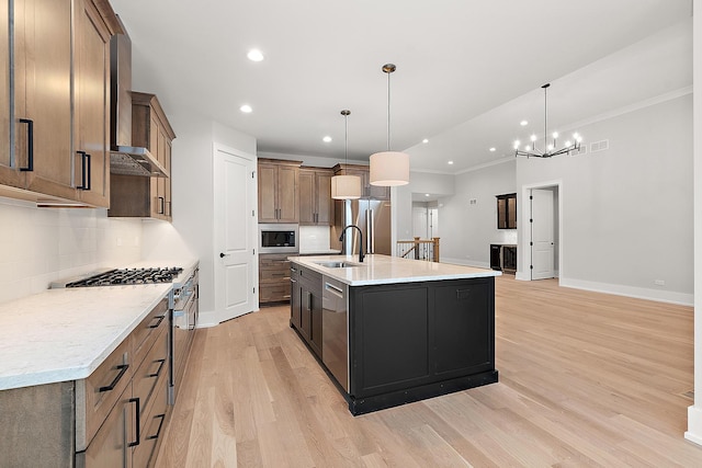 kitchen featuring a sink, decorative backsplash, appliances with stainless steel finishes, wall chimney range hood, and light wood-type flooring