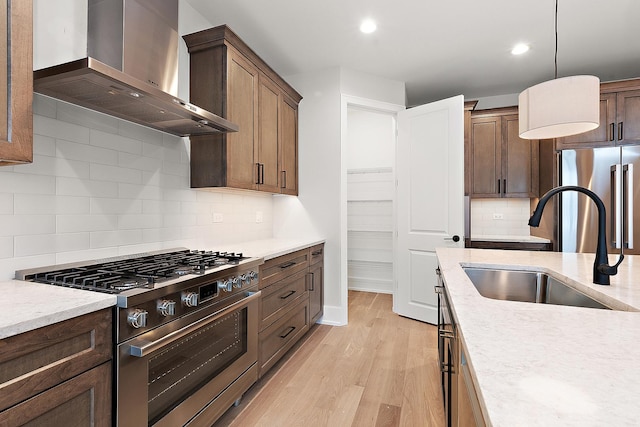 kitchen with decorative light fixtures, light wood-style floors, stainless steel appliances, wall chimney exhaust hood, and a sink