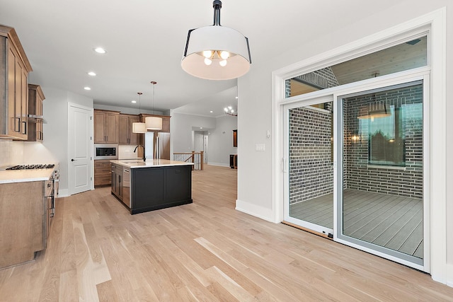 kitchen with a sink, light countertops, light wood-style floors, appliances with stainless steel finishes, and pendant lighting