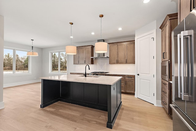 kitchen with a sink, hanging light fixtures, stainless steel appliances, light wood-type flooring, and backsplash