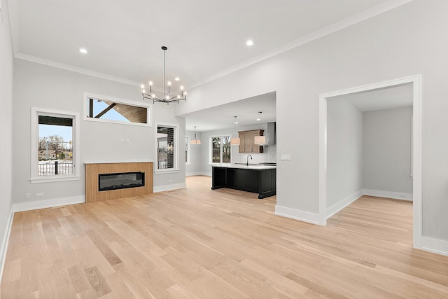 unfurnished living room featuring baseboards, an inviting chandelier, light wood-style flooring, a sink, and crown molding