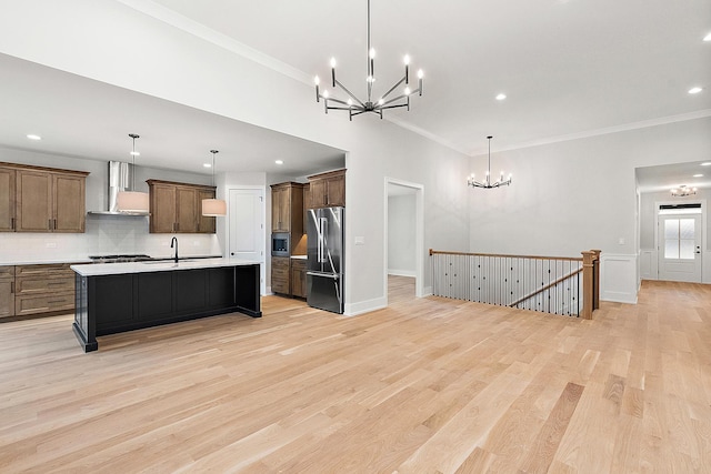 kitchen with light wood finished floors, an inviting chandelier, light countertops, appliances with stainless steel finishes, and wall chimney range hood