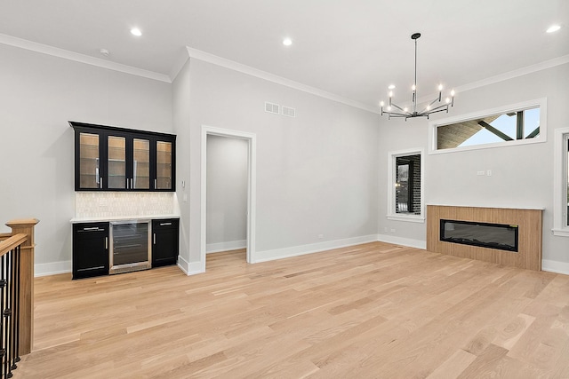 unfurnished living room with beverage cooler, light wood finished floors, an inviting chandelier, and ornamental molding