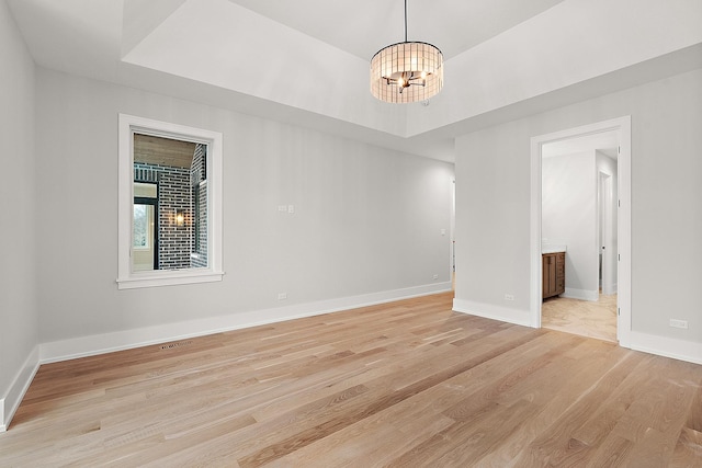 spare room featuring a tray ceiling, baseboards, a chandelier, and light wood finished floors