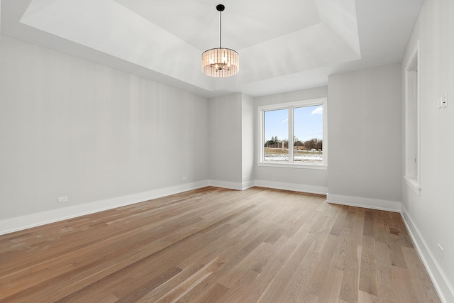 empty room featuring a tray ceiling, baseboards, light wood-style flooring, and a chandelier