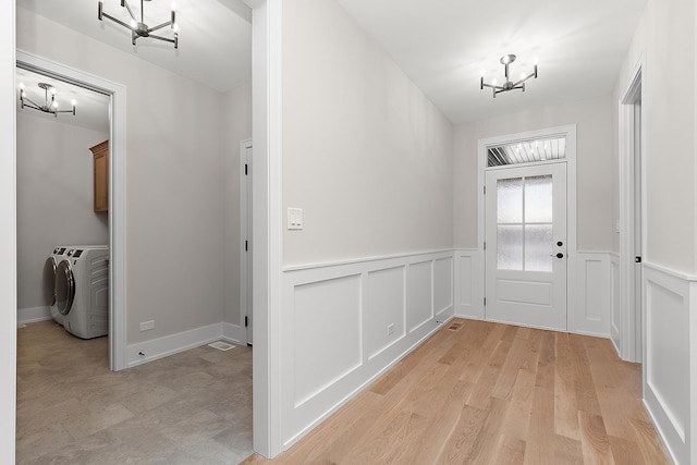 doorway to outside featuring washer and clothes dryer, a wainscoted wall, light wood-style floors, and an inviting chandelier