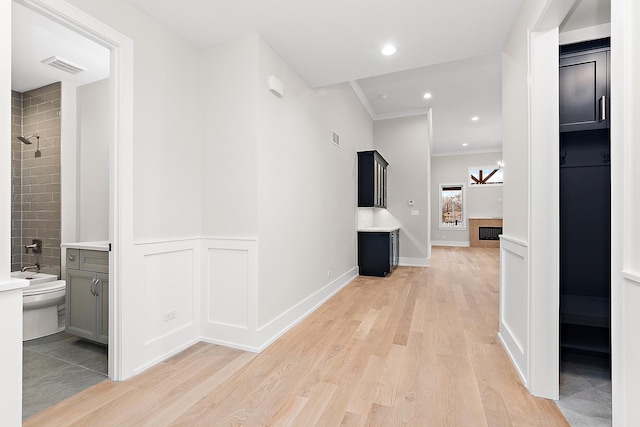 hallway featuring a wainscoted wall, visible vents, light wood-style flooring, recessed lighting, and crown molding