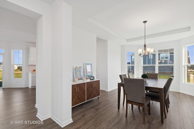 dining space with dark hardwood / wood-style flooring, a raised ceiling, and a notable chandelier