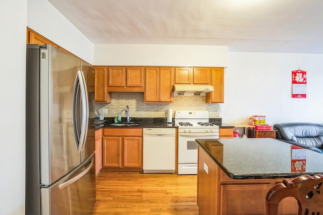 kitchen with light wood-type flooring, backsplash, white appliances, sink, and dark stone countertops