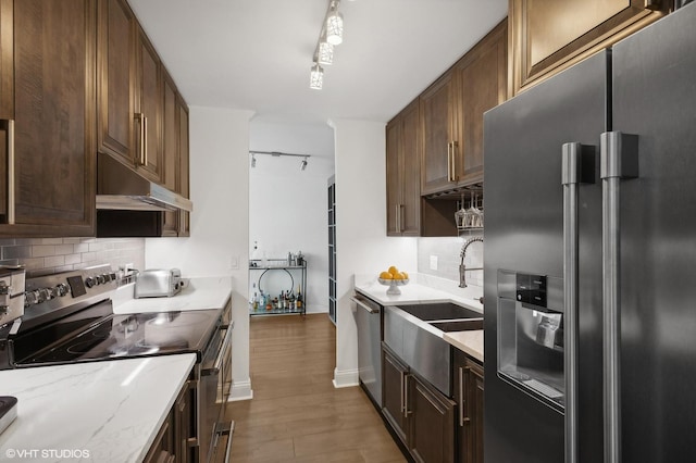 kitchen featuring dark wood-type flooring, sink, rail lighting, light stone counters, and stainless steel appliances