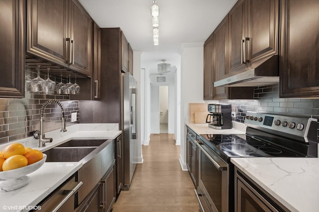 kitchen with sink, light stone counters, backsplash, dark brown cabinets, and appliances with stainless steel finishes