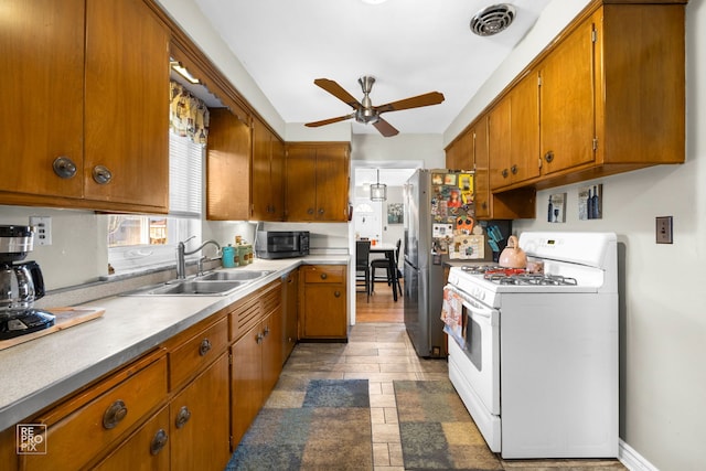 kitchen featuring stainless steel fridge, white gas stove, ceiling fan, and sink