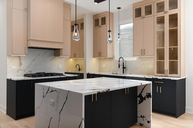 kitchen featuring light stone countertops, light brown cabinetry, sink, a center island, and hanging light fixtures